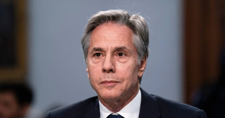 Former Secretary of State Antony Blinken gathering his belongings on a beach as a lifeguard stands nearby.